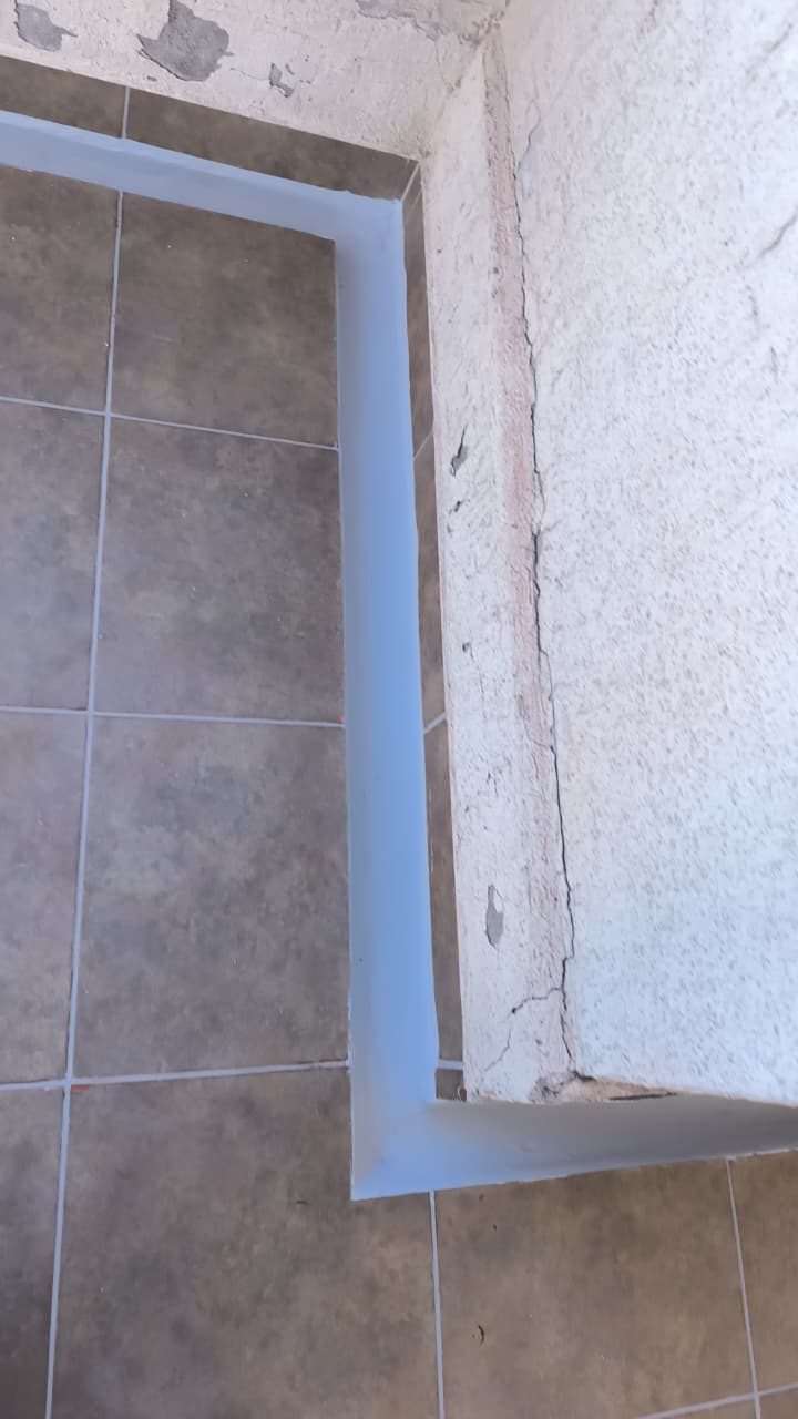 Sello elástico aplicado sobre una grieta en el encuentro de muro y piso de una terraza